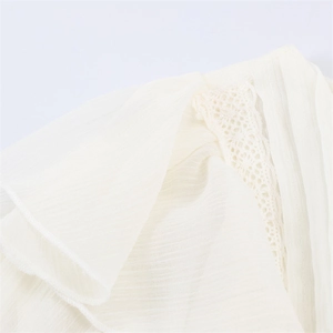 Close-up of ruffled layered trim and delicate lace hollow details on a cream blouse