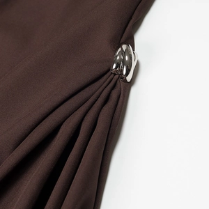 Detailansicht einer silbernen Metallschnalle auf einem dunkelbraunen Kleid mit Faltenwurf