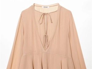 Detail of elegant V-neckline with adjustable tie-up ribbons on beige long sleeve shirt