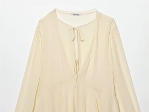 Detail of beige V-neck long sleeve blouse with lace-up ties and soft draped fabric