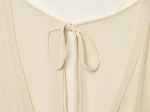 Close-up of beige blouse V-neckline with delicate bow-tie and decorative zigzag stitching