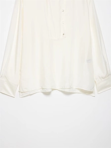 Detail of a creamy white silk shirt featuring a curved hem and polished front buttons