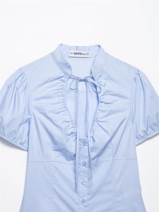 Dettaglio del colletto della camicia in popeline azzurro con fiocco e bottoni lucidi