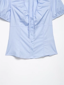 Dettaglio camicia in popeline azzurro con scollo a V, volant e fiocco decorativo