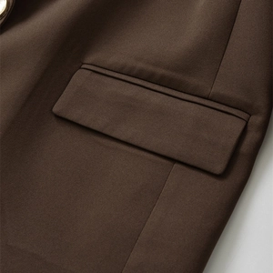 Nahaufnahme eines braunen Blazers mit goldenem Knopf und Taschendetail