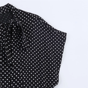 Detailed close-up of a women's black and white polka dot blouse with a neck tie bow