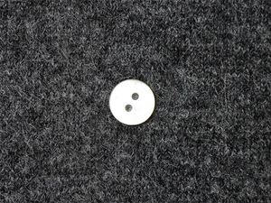Gros plan d'un bouton blanc nacré à deux trous sur une maille de couleur gris anthracite