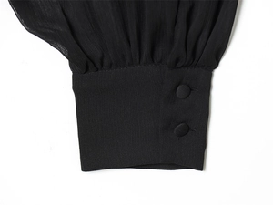Detail of elegant black blouse cuff with two fabric-covered buttons and fine texture