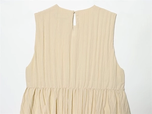 Détail de robe crème sans manches avec texture plissée et fermeture boutonnée au dos
