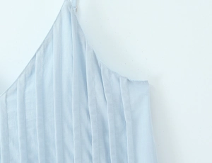 Close-up detail of light blue pleated fabric texture and thin strap on a summer dress
