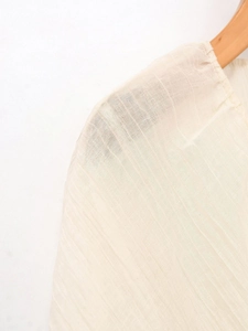 Dettaglio del tessuto beige della camicetta con trama a pieghe naturali e cuciture rifinite