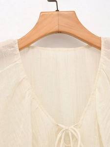 Dettaglio della trama della camicetta bianco crema con scollo a V e nastro decorato