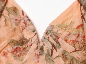 Detail of V-neckline with pleated texture and peach bird floral print on woven fabric