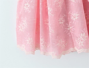 Dettaglio dell'orlo dell'abito rosa con ricamo floreale bianco e bordi in pizzo