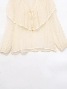 Dettaglio della camicetta beige con colletto a balze in pizzo e design con lacci al collo