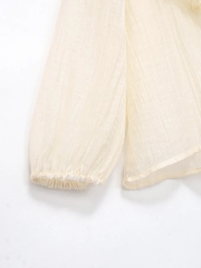 Dettaglio del tessuto plissettato beige chiaro con polsini elastici e bordi a balze
