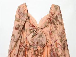 Detailed view of V-neckline with bow tie and peach floral bird print on woven fabric