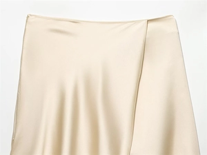Macro detail of champagne gold satin wrap skirt showing smooth glossy silk-like texture
