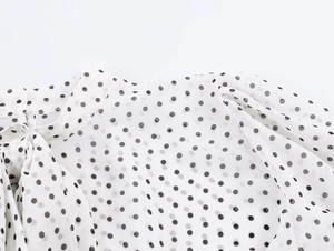 Détail d'un chemisier blanc à pois avec col à nœud papillon et manches bouffantes