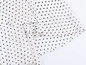 Détail des coutures et de l'étiquette d'entretien sur une blouse blanche à pois