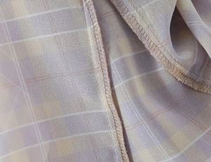 Dettaglio macro del tessuto in chiffon a quadri lavanda con cucitura overlock professionale