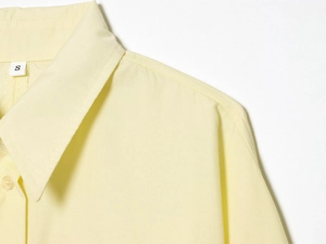 Detail shot of the pale yellow cotton polo shirt collar and shoulder with size label S