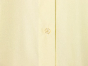 Close-up of a single yellow resin button on a light yellow cotton poplin shirt detail