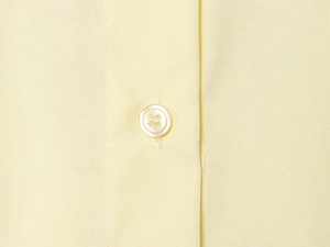 Macro detail of a pale yellow poplin shirt featuring a white button and fine fabric texture