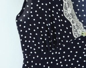 Detail of navy polka dot dress with white lace trim V-neck and small green bow
