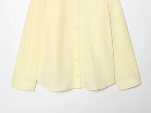 Detail of pale yellow poplin shirt showing white buttons and curved hemline