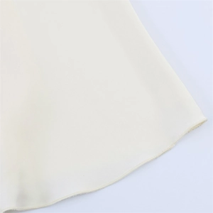 Detailed close-up of the curved hemline with premium overlock stitching on cream dress