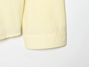 Close-up of the fine stitching on the cuffs of a light yellow poplin long sleeve shirt