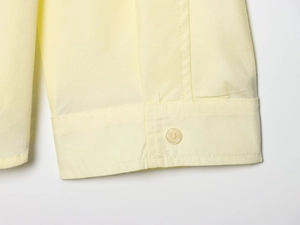 Detail of pale yellow cotton shirt cuff featuring neat stitching and single button