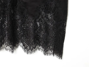 Close-up of black satin fabric with delicate eyelash floral lace trim at the hemline