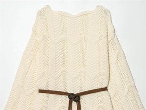 Détail d'un pull en maille blanc cassé montrant la texture ondulée et la ceinture à pompons