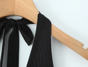 Gros plan sur le détail des brides d'un haut dos nu en maille noire sur cintre en bois