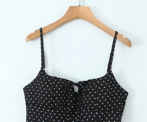 Detail of black polka dot camisole top featuring a bow tie and slim straps on a wooden hanger