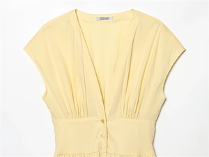 Detail of light yellow V-neck poplin dress featuring pleated waist and button closure