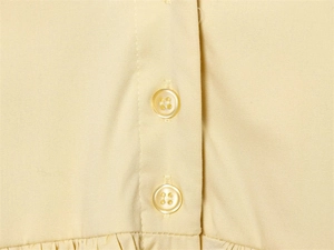 Detailed close-up of buttons and fabric texture on a light yellow poplin mini dress