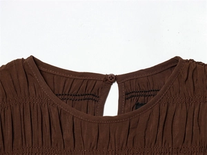 Close-up of dark brown dress neckline with back button closure and pleated fabric details