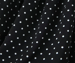 Detailed macro view of black chiffon fabric with white polka dots and soft pleated texture