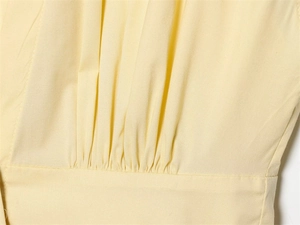 Close-up of pale yellow poplin dress featuring detailed ruched seams and fine fabric texture