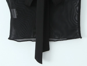 Détail de maille noire montrant la texture douce et un ruban élégant sur le vêtement