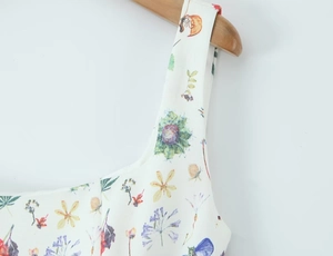 Detail of floral print summer dress shoulder straps on a wooden hanger background