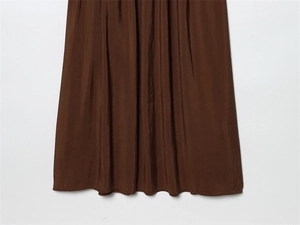 Detail view of the brown satin dress hem showing high-quality draping and pleated texture