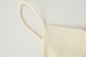 Detail of thin shoulder strap and cream fabric texture on a modern asymmetric dress