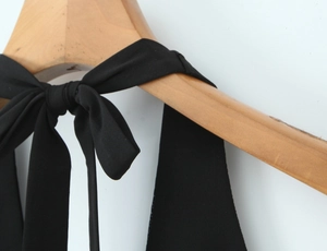 Détail de l'encolure licou avec nœud et tissu noir texturé sur un cintre