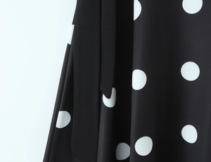 Gros plan sur tissu noir à pois blancs avec détail de lien à nouer assorti du haut