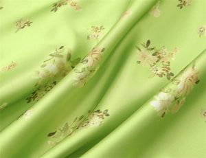 Close-up of light green floral silk fabric with smooth satin texture and elegant drape
