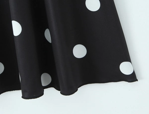 Détail du tissu noir à pois blancs montrant les coutures de l'ourlet et le drapé fluide